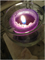 purple lit candle in round glass holder
